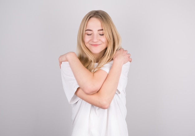 Portrait of lovely cheerful girl hugging herself enjoying herself on grey