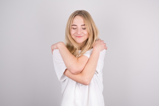 Portrait of lovely cheerful girl hugging herself enjoying life isolated on gray background