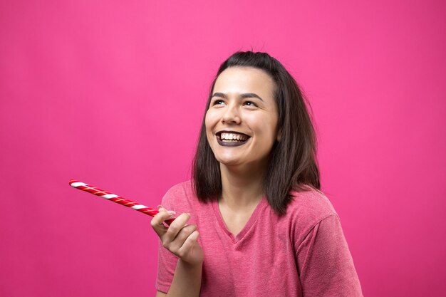 Portrait of lovely cheerful woman with straight brown hair trying to bite red candy cane christmas