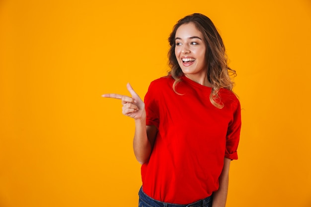 Ritratto di una giovane donna allegra adorabile in piedi isolata sul muro giallo, presentando lo spazio della copia