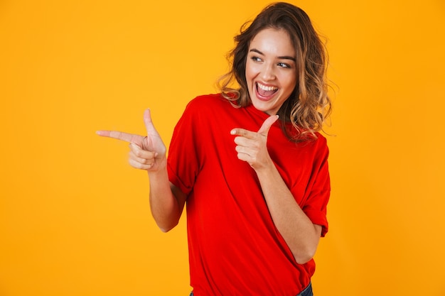 Portrait of a lovely cheerful young woman standing isolated over yellow wall, presenting copy space