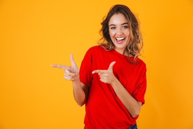 Portrait of a lovely cheerful young woman standing isolated over yellow wall, presenting copy space