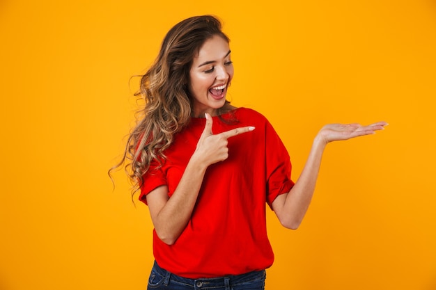 Portrait of a lovely cheerful young woman standing isolated over yellow wall, presenting copy space