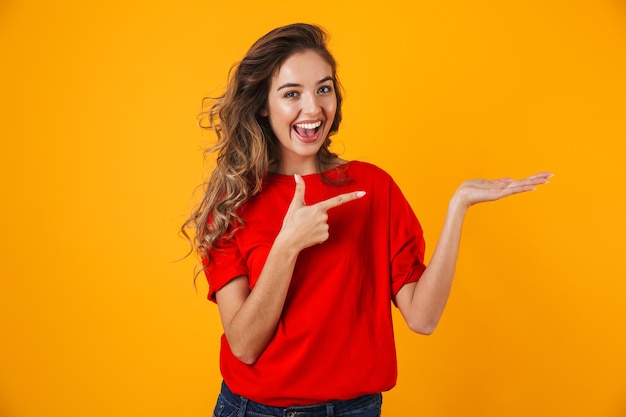 Portrait of a lovely cheerful young woman standing isolated over yellow wall, presenting copy space