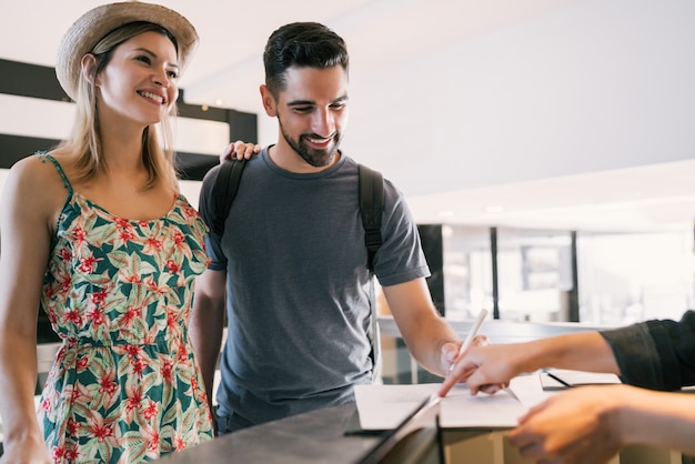 Portrait of lovely couple doing check-in at hotel reception front desk. Holiday and travel concept.