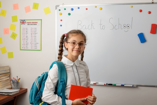 バックパックと本の教室で立っているガラスの素敵な女の子の肖像画