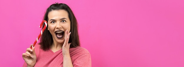 Ritratto di una bella donna allegra dolce e adorabile con capelli castani dritti che cerca di mordere una caramella rossa