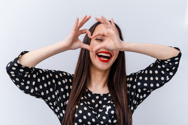 Portrait of a lovely woman making heart with fingers. White background.