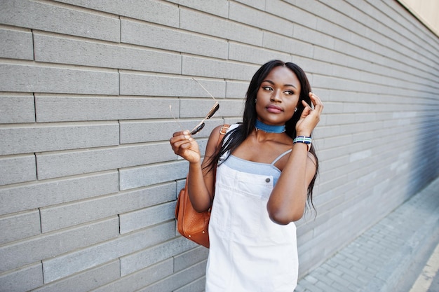 Portrait of a lovely young african american woman posing with sunglasses against a brick wall in the background