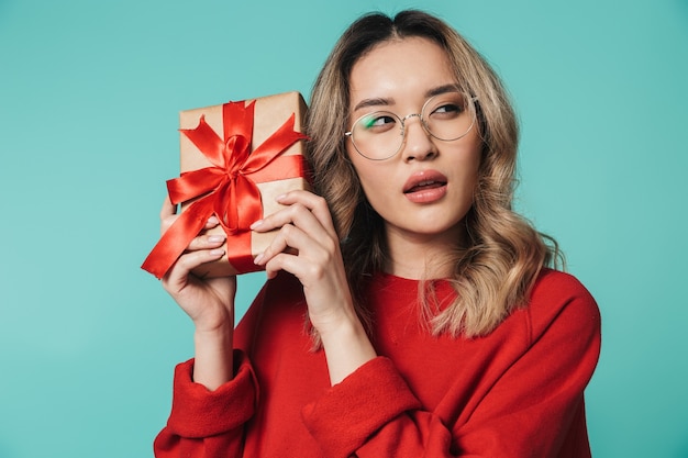 Portrait of a lovely young asian woman standing isolated over blue wall, showing present gift box