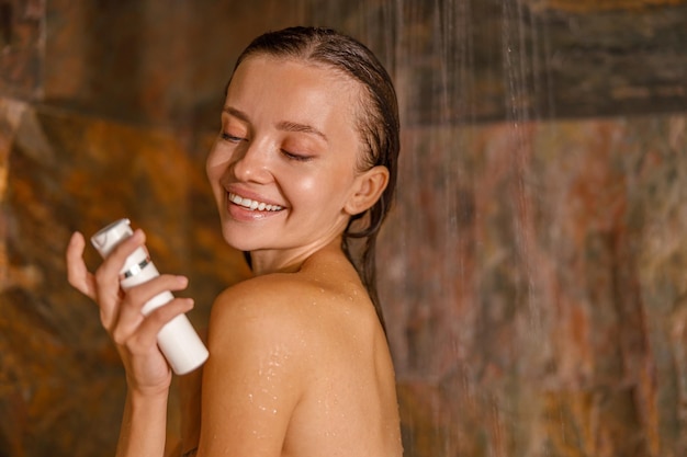 Portrait of lovely young woman standing in marble shower and washing her body using organic natural