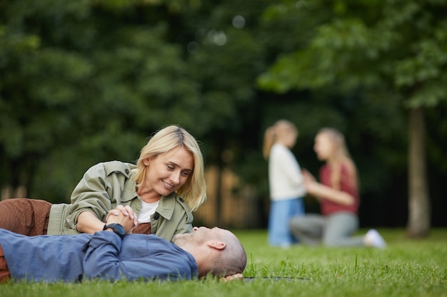 Portrait of loving adult couple laying on green grass in park and enjoying time together outdoors