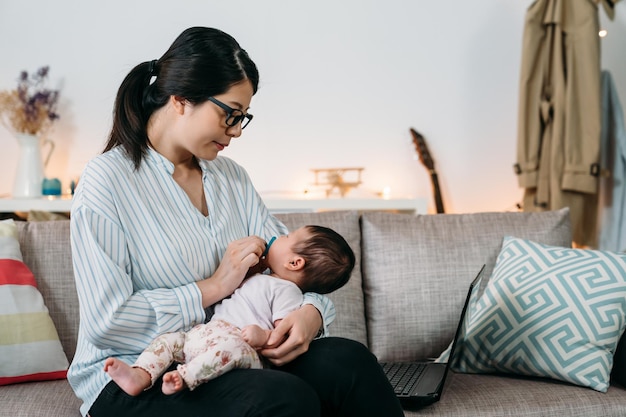 Photo portrait loving asian career mother working from home is comforting her newborn baby to sleep while keeping her hand on the pacifier in the living room.