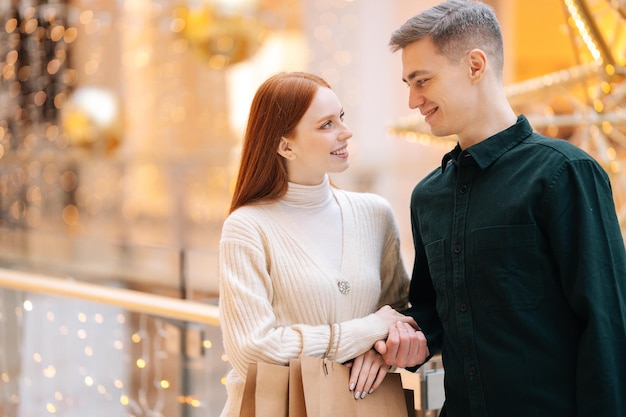 Portrait of loving beautiful young couple holding shopping bags standing in mall and looking at each