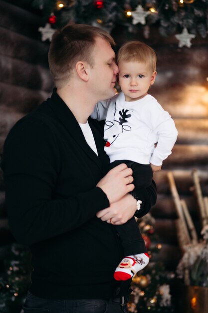 Portrait of loving dad with son on his shoulders decorating beautiful Christmas tree with toys and decoration at home