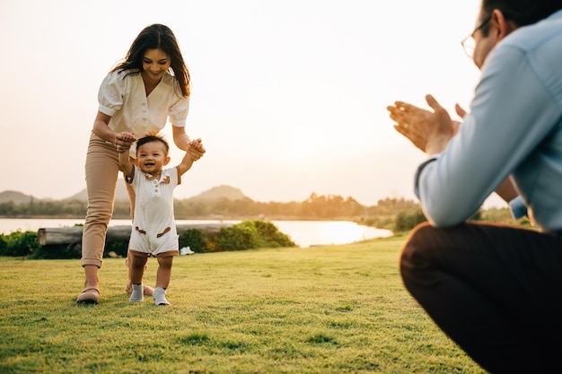 Portrait of a loving family spending quality time in nature, teaching their baby girl to walk on a beautiful spring day. childhood parent care support concept