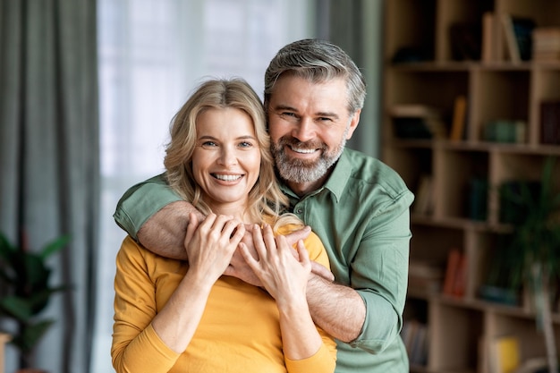 Photo portrait of loving middle aged spouses embracing and smiling at camera