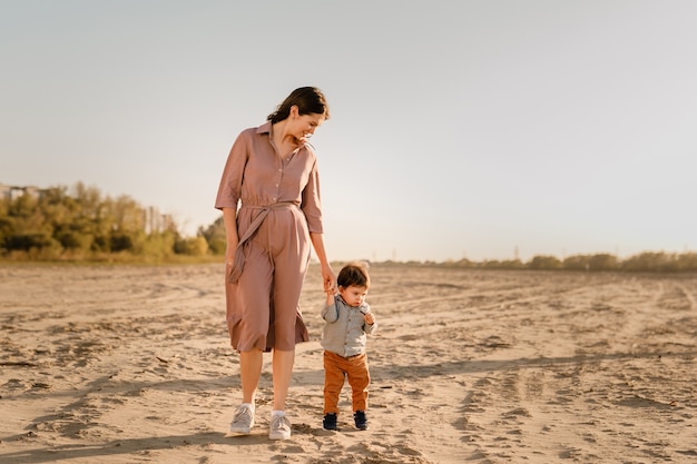 Ritratto di madre amorevole e suo figlio di un anno che camminano e giocano con la sabbia.