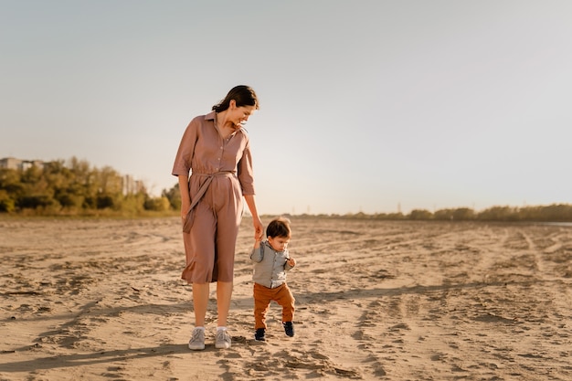 Portrait of loving mother and his one years old son walking and playing with sand.