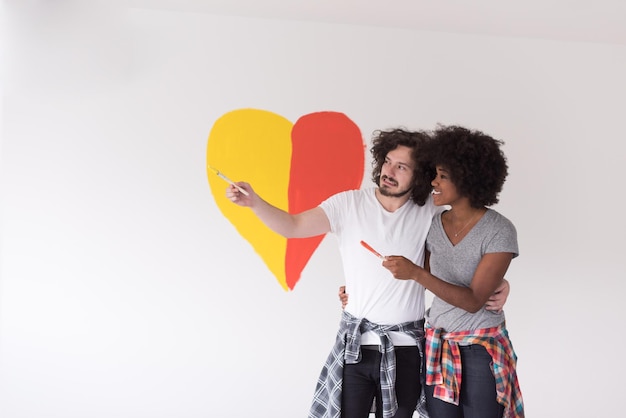 Portrait of loving multiethnict couple with painted heart on wall