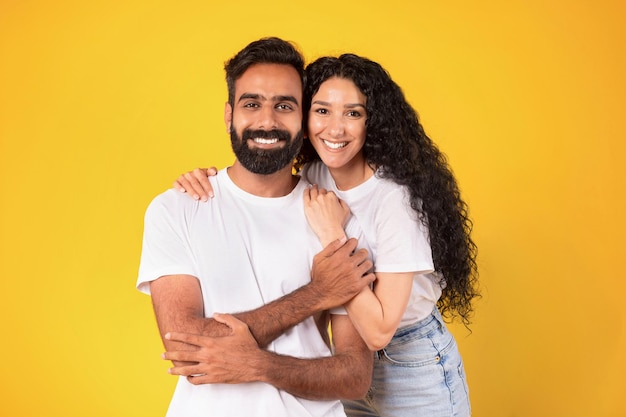 Portrait of loving young arabic spouses hugging over yellow background