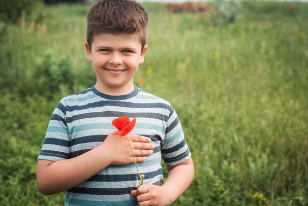 Ritratto di un ragazzo dolce e fortunato con un fiore di papavero rosso il bambino preme un fiore di campo al suo cuore