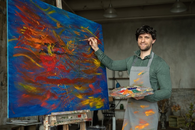 Portrait of male artist working on painting in studio male artist makes strokes with yellow paint