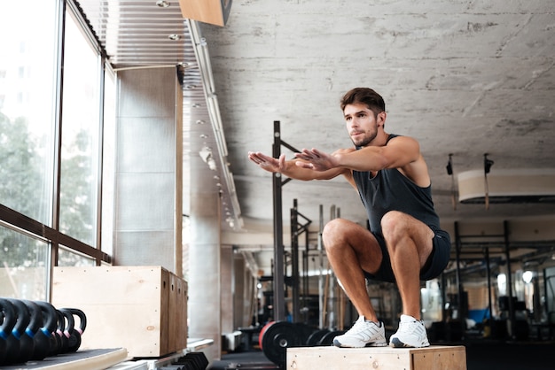Portrait of male athlete standing on wooden box in gym