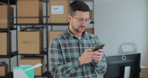 Portrait of male business owner using smartphone at work in warehouse A man connects to customer support via the Internet Work manager in an online store