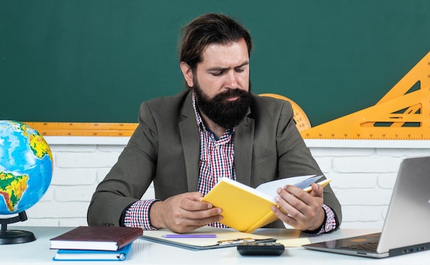 Portrait Of Male College Student With Book Sitting In Classroom Alone reading