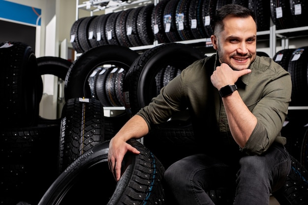 Portrait of male customer surrounded by many car tires making choice and purchase. sits alone posing at camera.