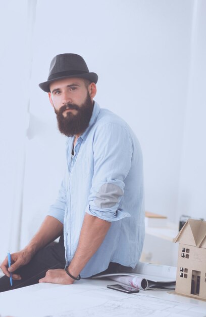 Portrait of male designer in hat with blueprints at desk