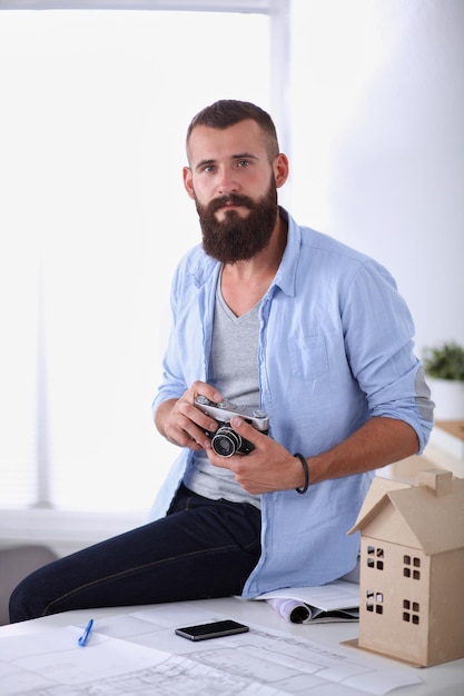 Portrait of male designer with blueprints at desk in office, isolated