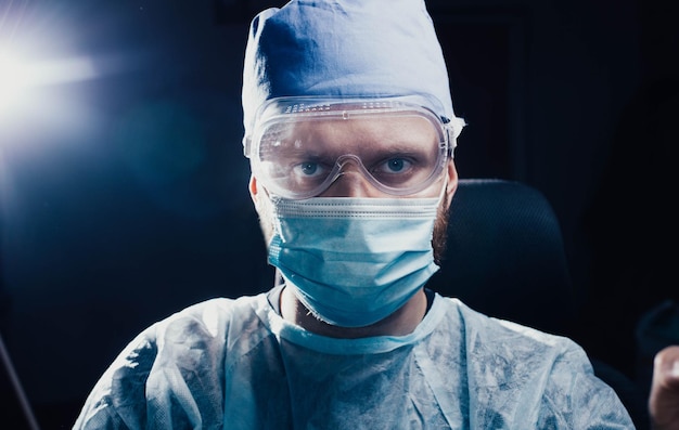 portrait of a male doctor in a mask glasses and uniform on a dark background medic works in the of