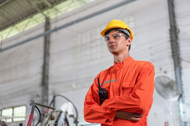 Portrait of male engineer in orange uiform cross arms standing at factory Industrial