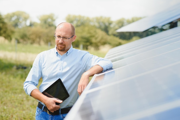 Portrait of male engineer with tablet in his hands near the solar panels station wearing helmet at sunny day Green ecological power energy generation