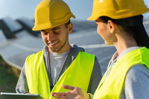 Portrait of the male and female engineers using tablet to control photovoltaic panels remotely during work on solar farm on sunny day