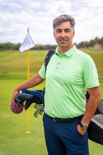 Portrait of male golfer walking down fairway carrying bags playing golf