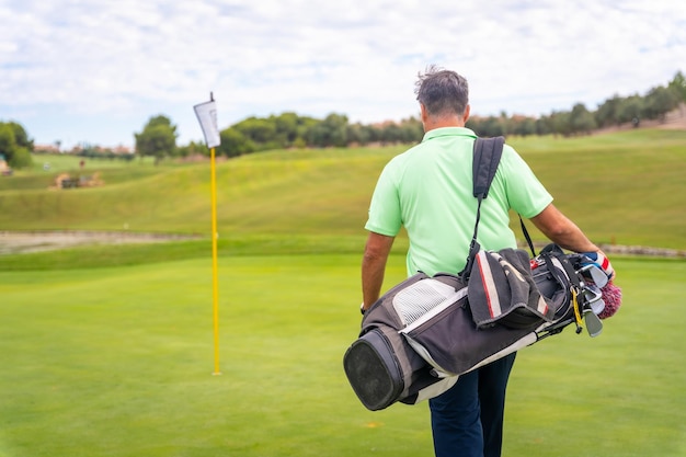 Portrait of male golfer walking down fairway carrying bags playing golf