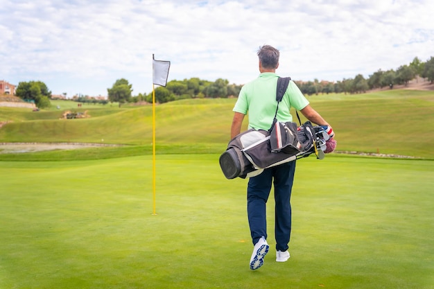 Portrait of male golfer walking down fairway carrying bags playing golf