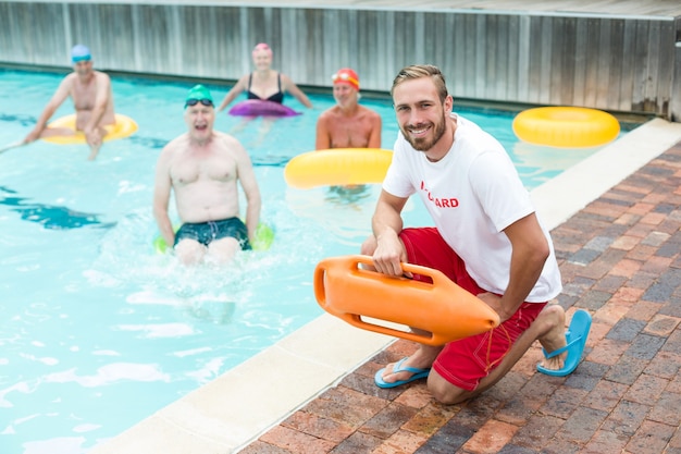 Portrait of male lifeguard crouching while swimmers swimming in pool