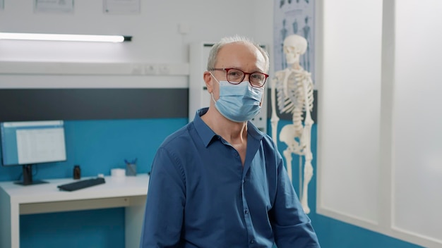 Portrait of male patient waiting to do consultation with doctor\
during coronavirus pandemic. elder man attending checkup\
examination to receive medical assistance and support in\
office.