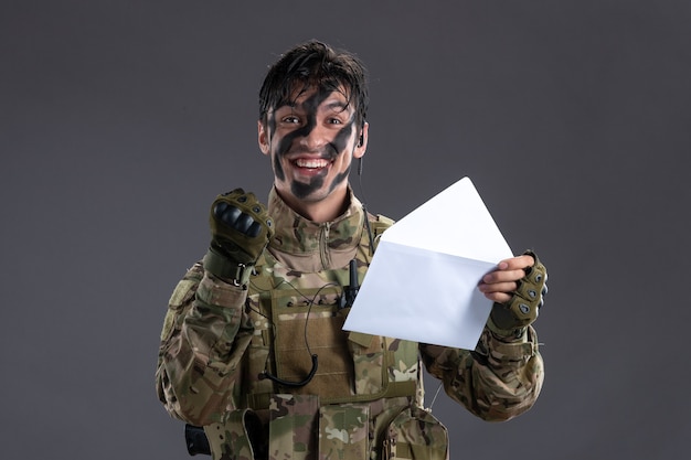 Portrait of male soldier in camouflage holding letter on dark wall