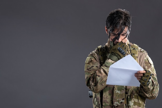 Photo portrait of male soldier in camouflage received letter on dark wall