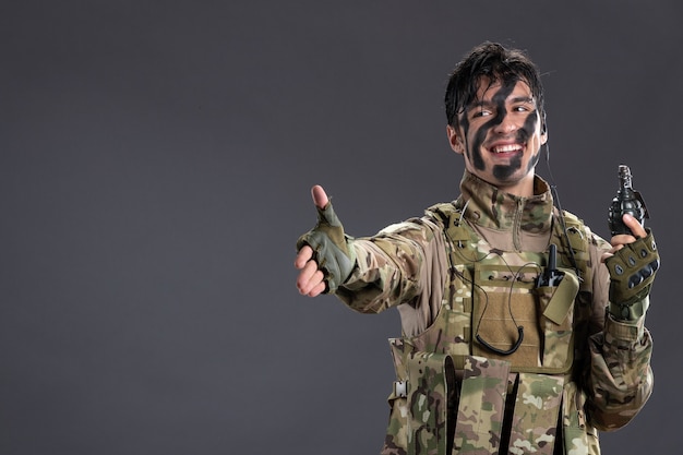 Portrait of male soldier in camouflage with grenade on a dark wall