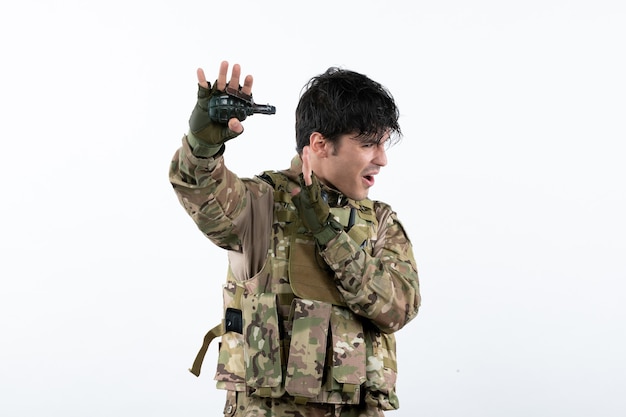 Portrait of male soldier in military uniform with grenade on white wall