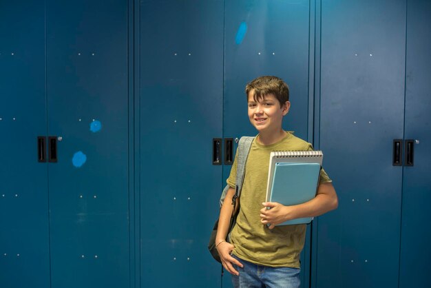 Photo portrait of male student holding books while standing against lockers