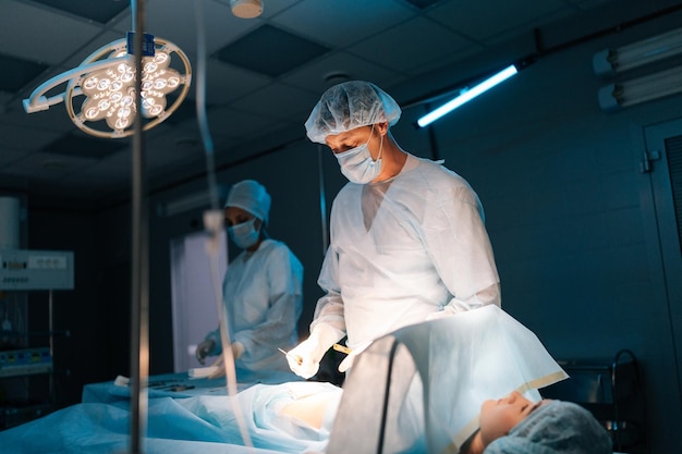 Portrait of male surgeon and african female nurse performing operation under electric lamp in dark