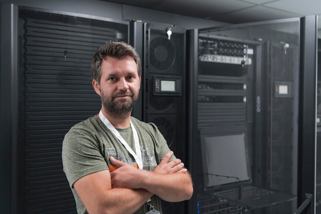 Portrait of male technician or network administrator standing brave as a hero with arms crossed in data center server room. High quality photo