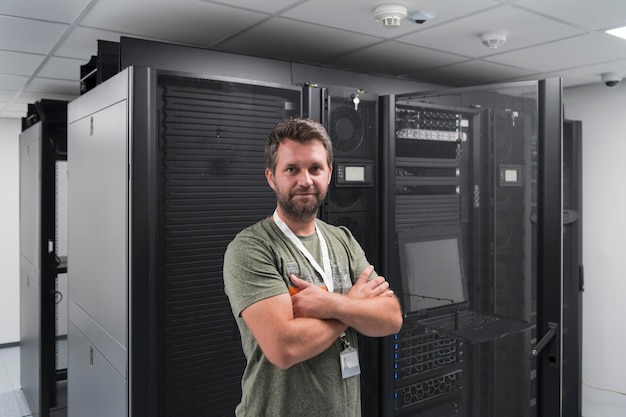 Portrait of male technician or network administrator standing\
brave as a hero with arms crossed in data center server room. high\
quality photo